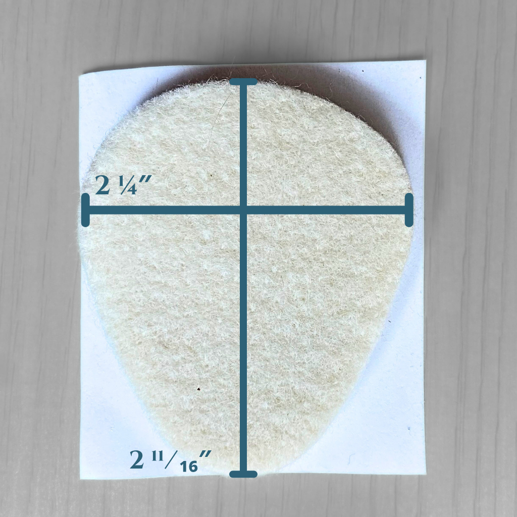 A teardrop-shaped off-white adhesive felt metatarsal pad pad shown on a white backing card, with dark teal measurement lines and text indicating dimensions of 2 1/4 inches wide and 2 1/16 inches tall, placed on a light wood surface.